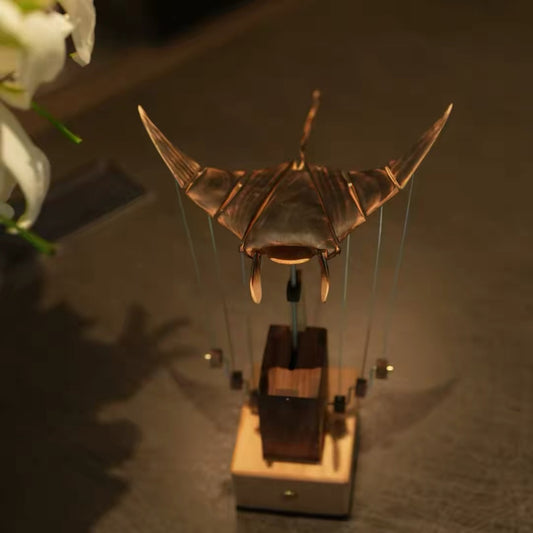 Front view of a wooden manta ray automaton displayed on its mechanical base in warm ambient light.