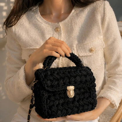 Black crochet top handle shoulder bag with gold clasp held by a model wearing a white textured jacket