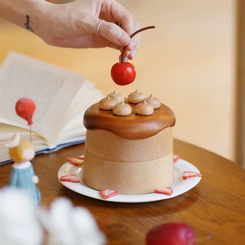 Hand holding the red cherry topper above the layered wooden jewelry box