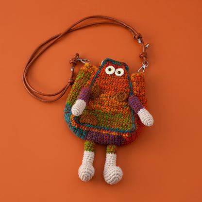 Colorful handwoven crochet character crossbody bag with cute eyes, arms and legs on an orange background.