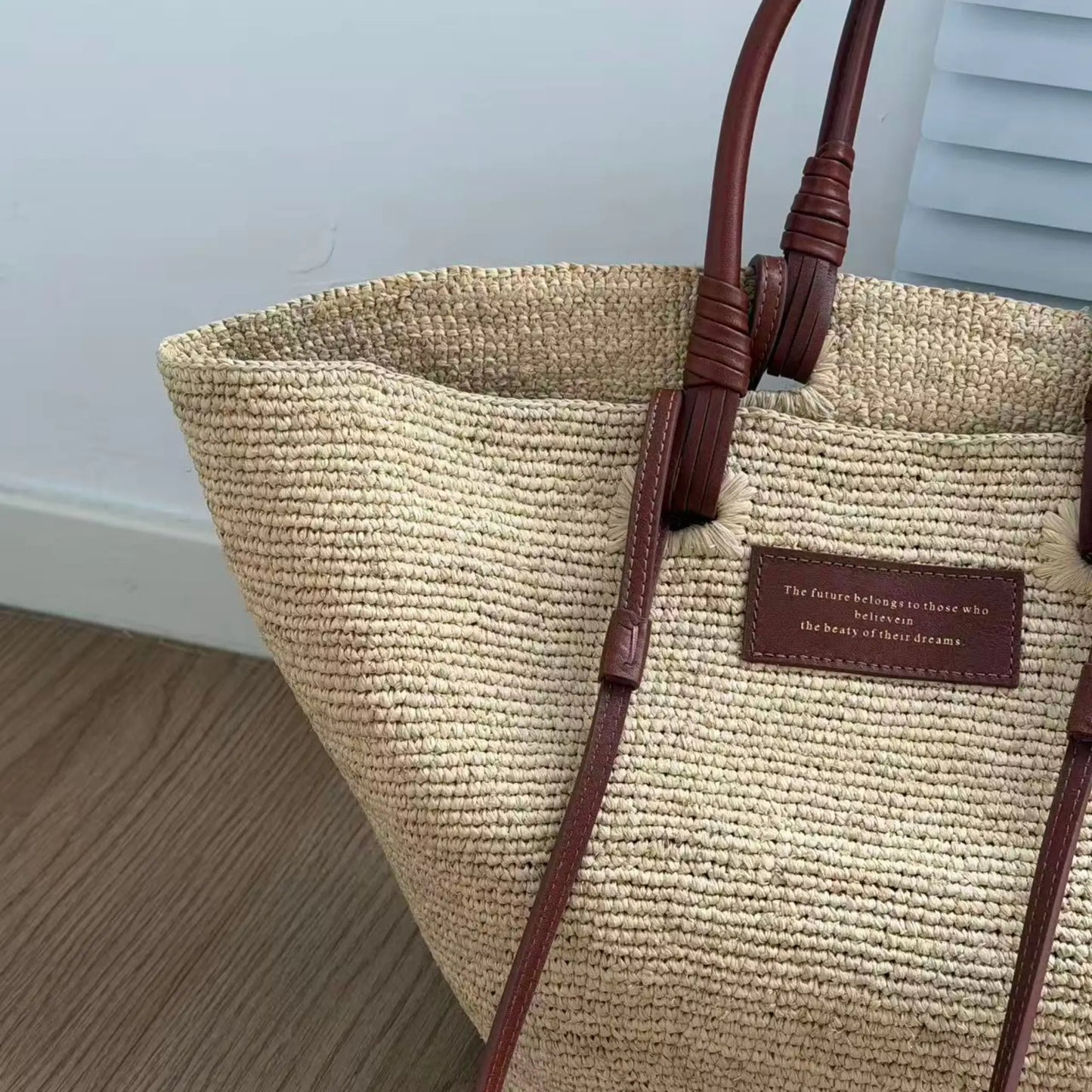 Close-up of a handmade raffia tote bag with brown leather handles, showing the natural woven texture and artisanal basket bag details