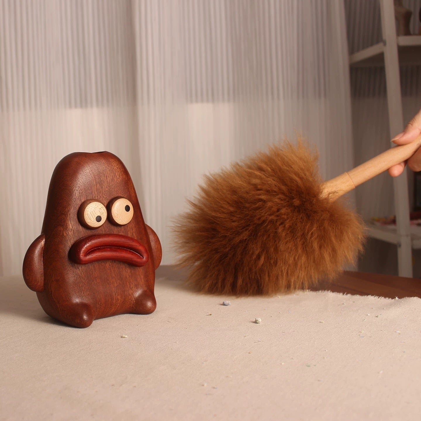 Brown lambswool duster cleaning a tabletop beside its pouty wooden character holder.