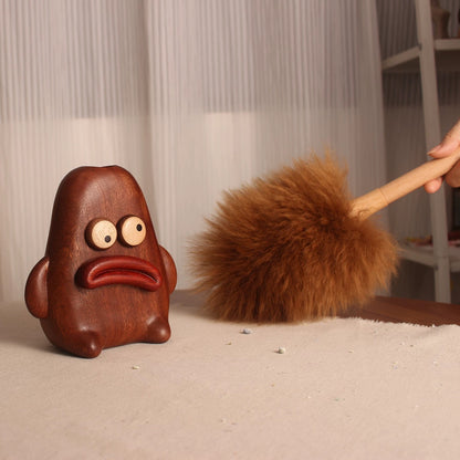 Brown lambswool duster cleaning a tabletop beside its pouty wooden character holder.