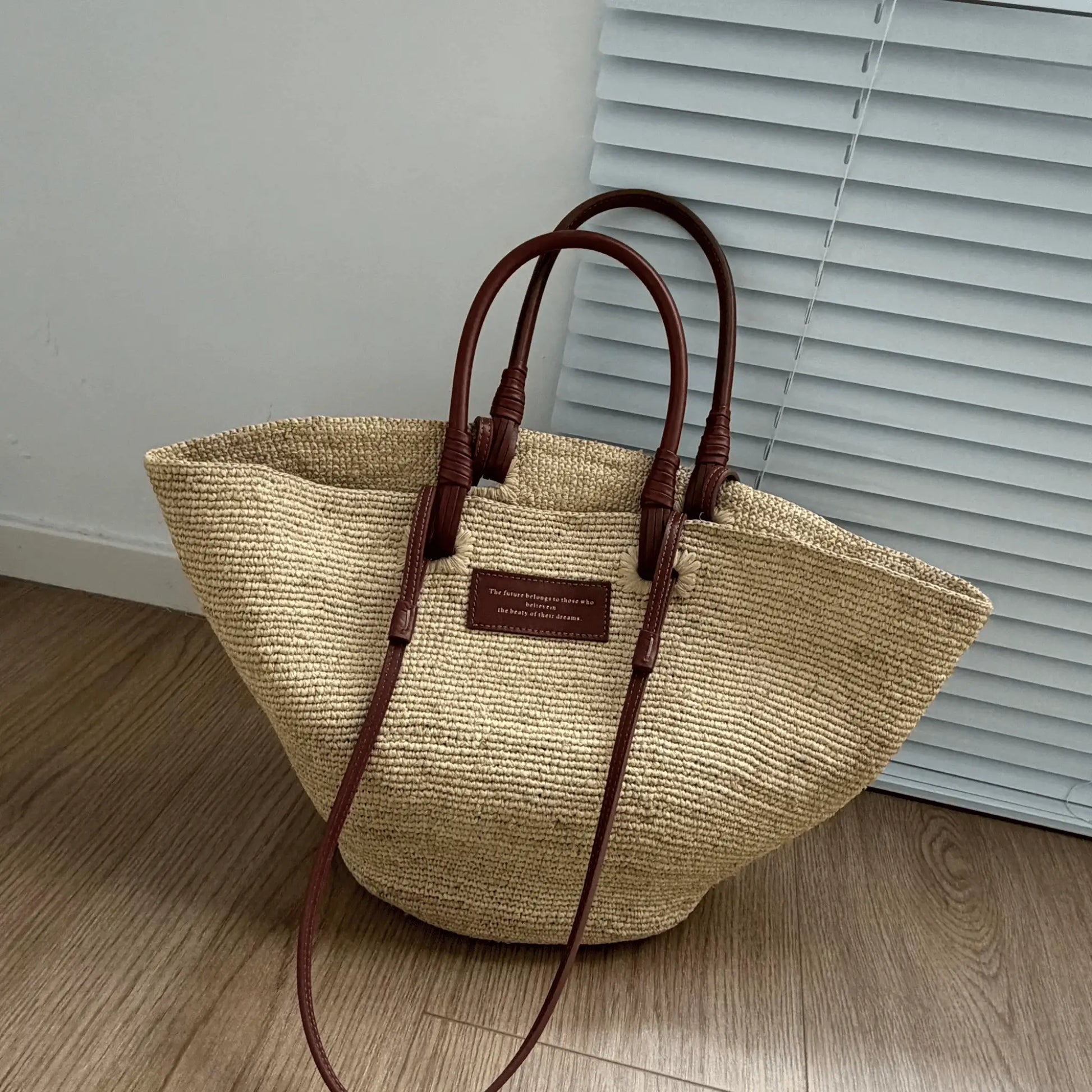 Large handmade raffia tote bag with brown leather handles and natural straw texture, designed as a stylish beach tote or everyday summer bag