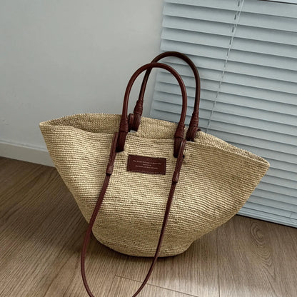 Large handmade raffia tote bag with brown leather handles and natural straw texture, designed as a stylish beach tote or everyday summer bag