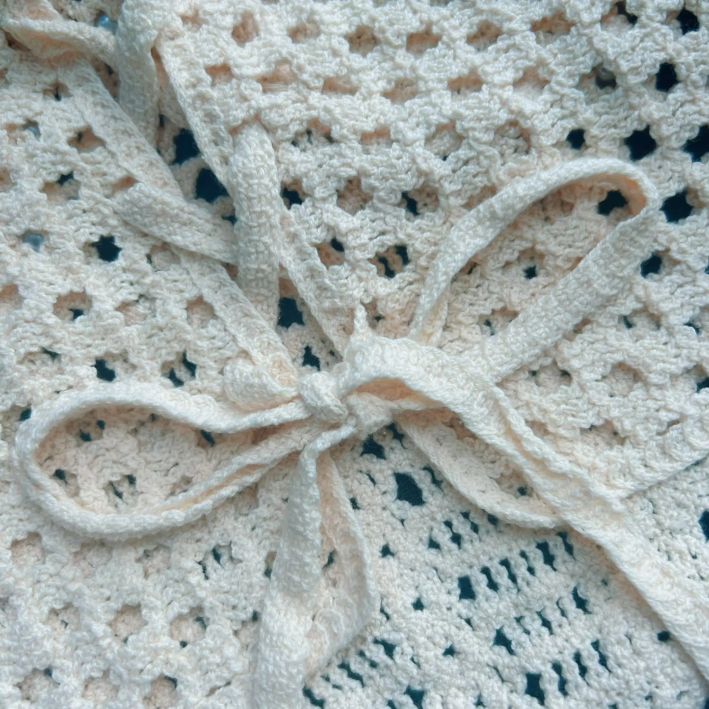 Close-up of the back tie detail on a cream crochet set, featuring openwork knit texture, delicate straps, and handmade crochet pattern