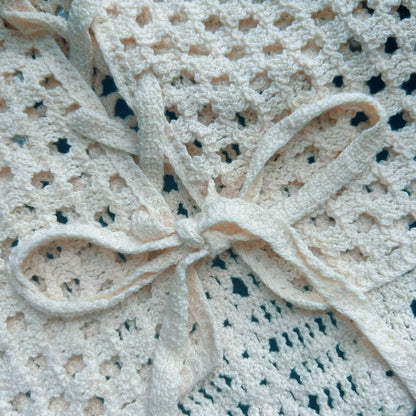 Close-up of the back tie detail on a cream crochet set, featuring openwork knit texture, delicate straps, and handmade crochet pattern
