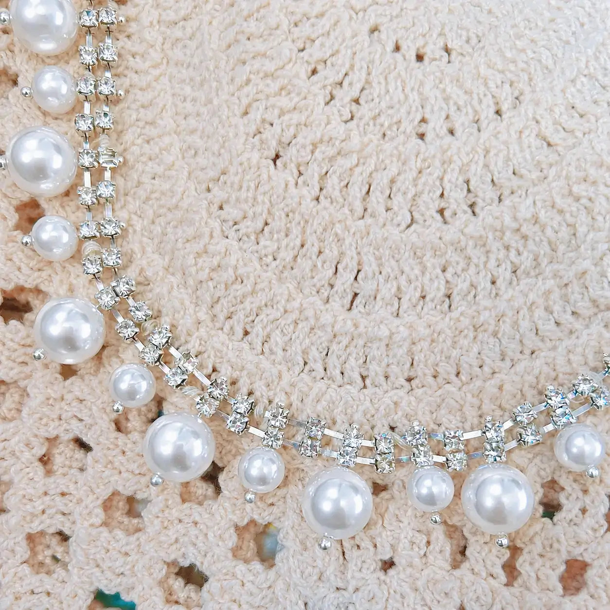 Close-up detail of a cream crochet top featuring glossy pearl embellishments and sparkling rhinestone trim