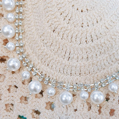 Close-up detail of a cream crochet top featuring glossy pearl embellishments and sparkling rhinestone trim