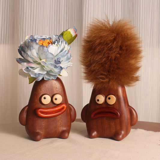 Two quirky wooden characters shown as a flower vase and a brown lambswool duster for playful tabletop decor.