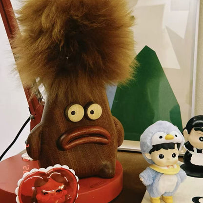 Quirky wooden lambswool duster displayed as playful desk decor beside collectibles and a red lamp.