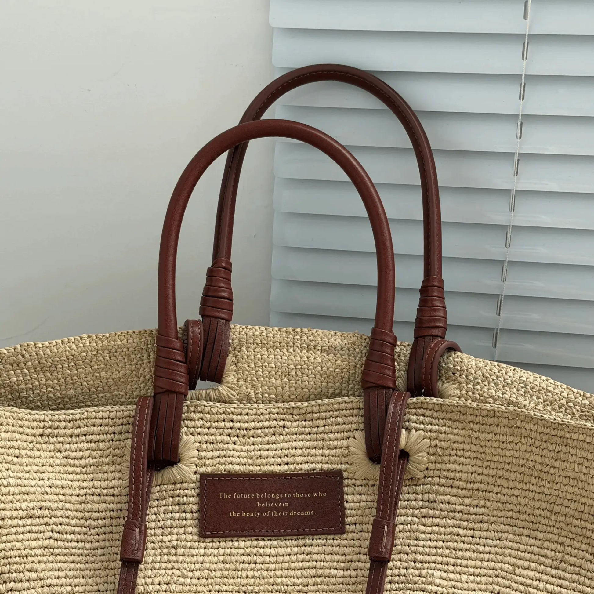 Detail shot of a raffia basket tote bag with brown leather handles, woven raffia texture, and handmade summer bag craftsmanship