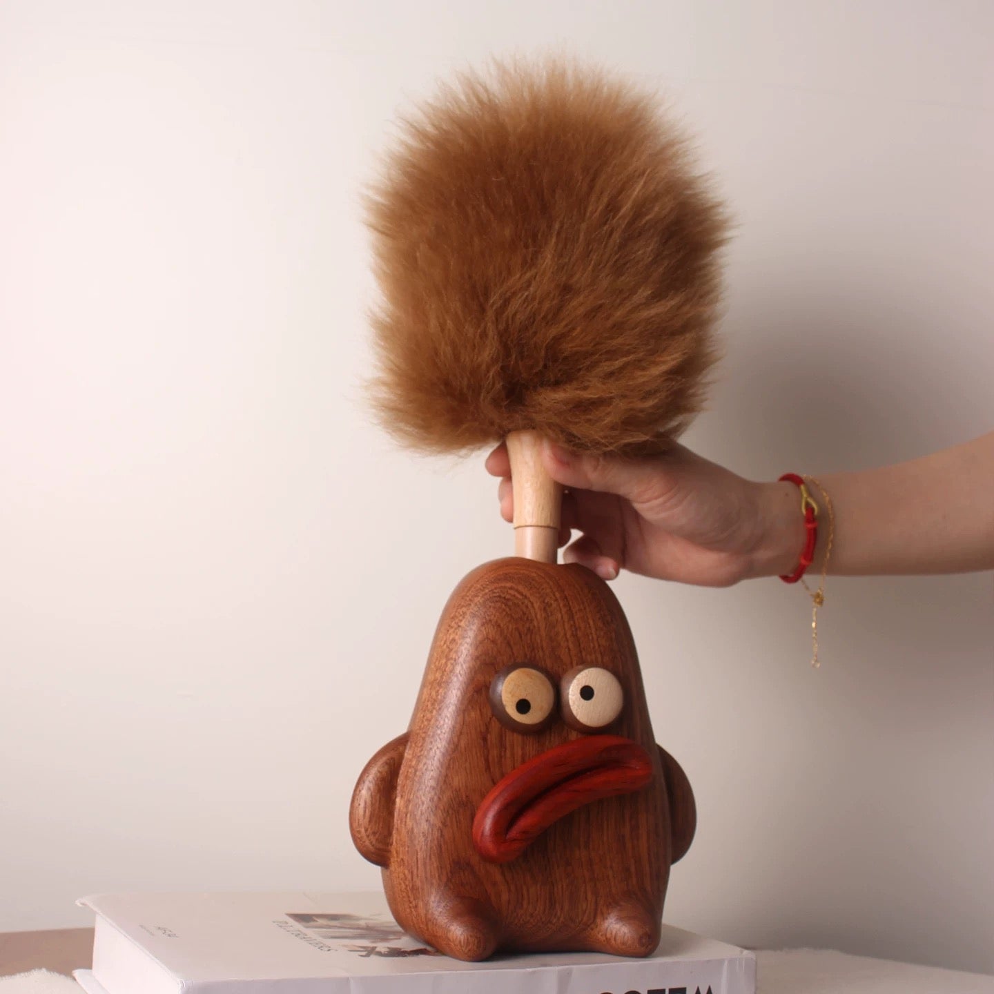Hand returning the removable brown lambswool duster to its pouty wooden character holder.