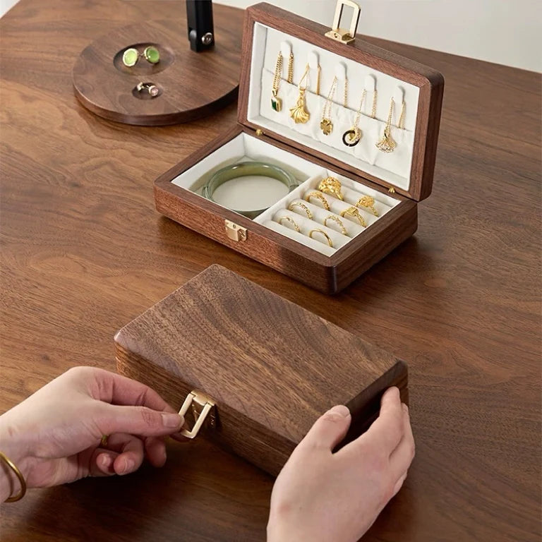 Hands opening the clasp of a walnut jewelry box beside an open single-layer box with ivory lining.