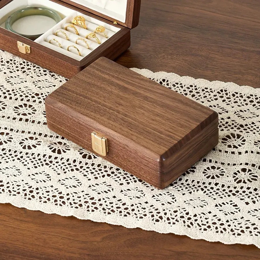 Closed walnut jewelry box showing natural wood grain, rounded corners and a gold-tone clasp.