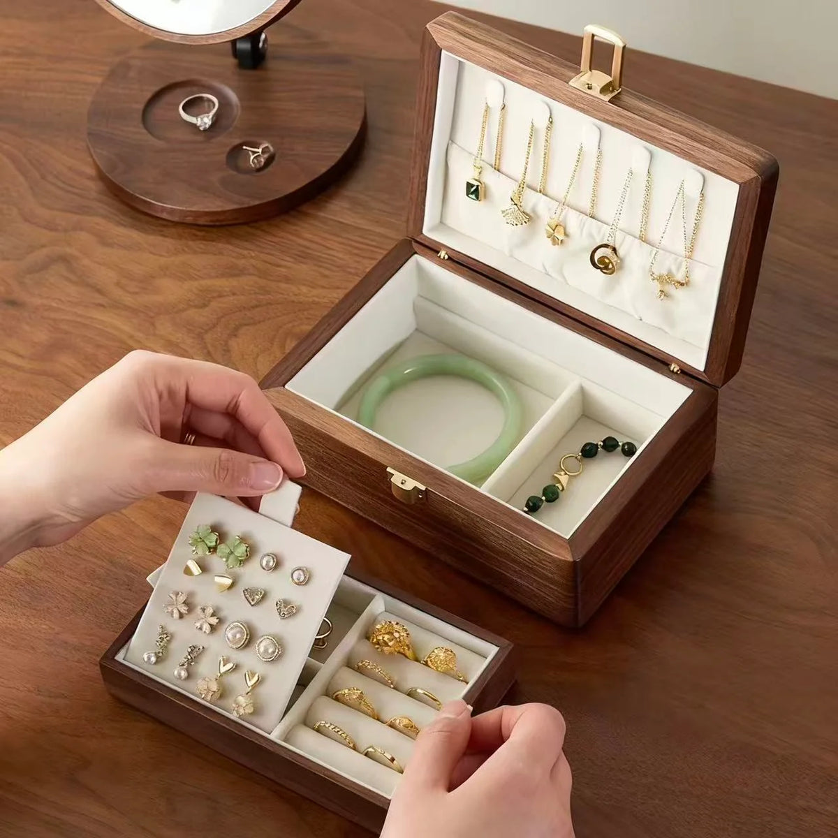 Hands lifting the ivory-lined tray from a double-layer walnut jewelry box to reveal the lower storage compartments.