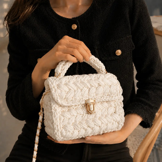 White chunky crochet top handle bag styled with a black outfit, featuring a gold clasp and woven chain strap.