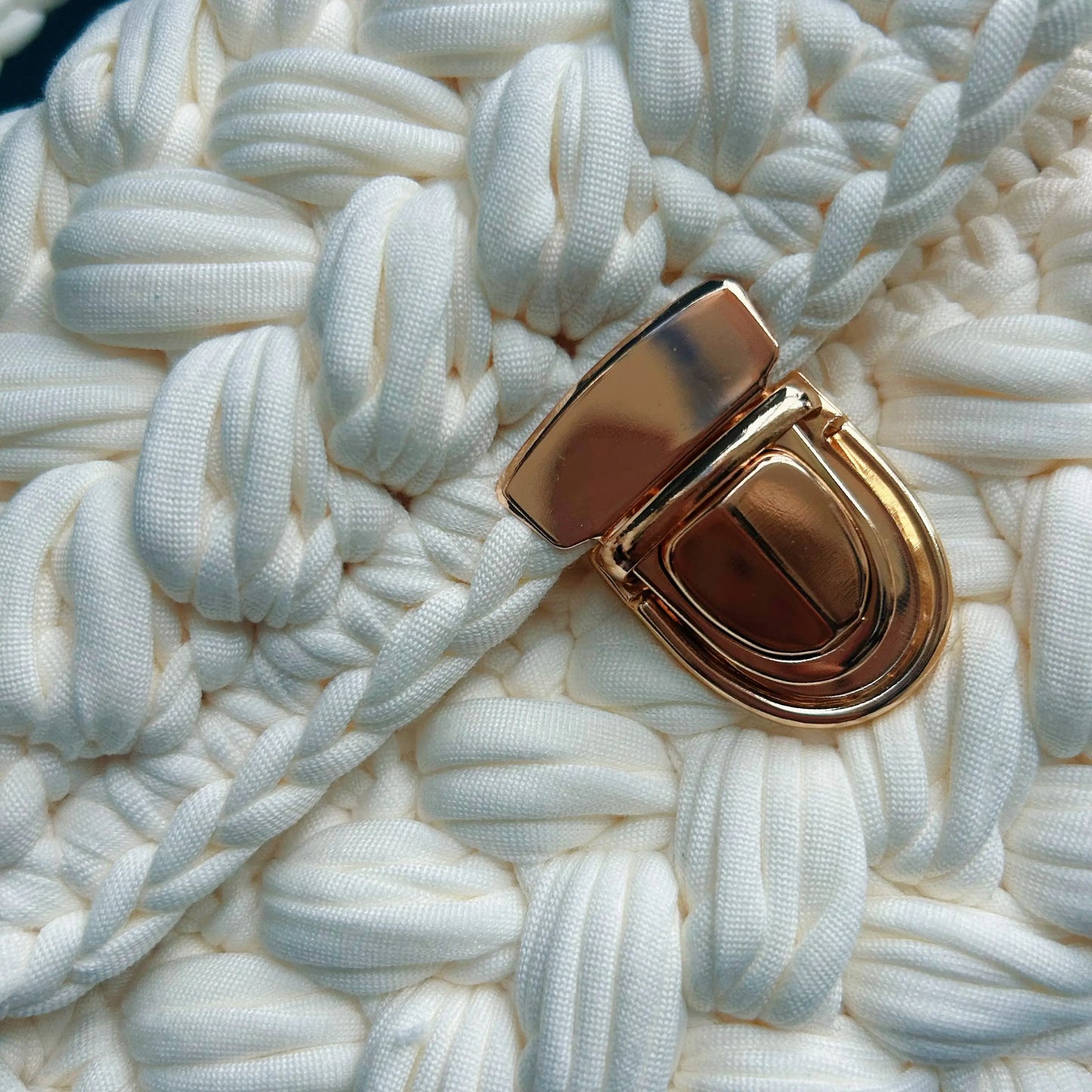 Close-up of the white chunky crochet bag showing the woven texture and polished gold push-lock clasp