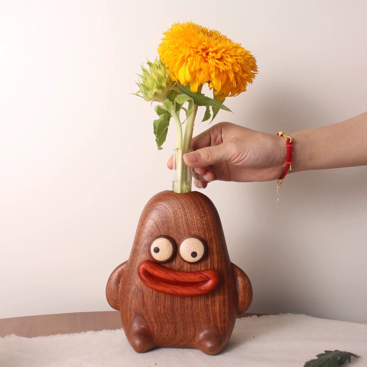 Hand placing orange flowers into the clear tube of a smiling wooden character bud vase.